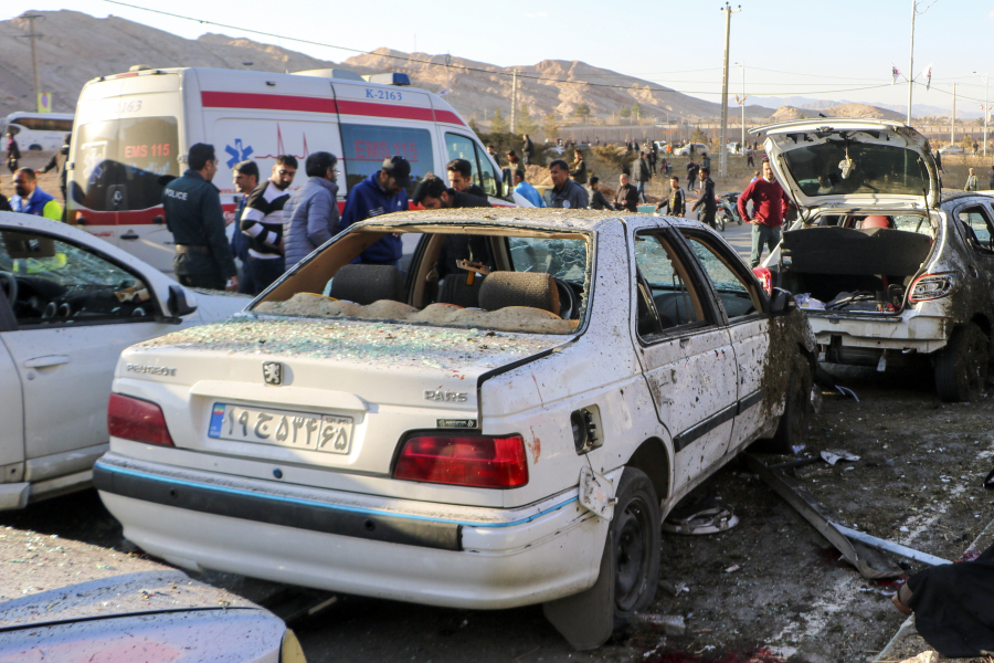 People stay next to destroyed cars after an explosion in Kerman, Iran, Wednesday, Jan. 3, 2024. Iran says bomb blasts at an event honoring a prominent Iranian general slain in a U.S. airstrike in 2020 have killed at least 103 people and wounded 188 others.