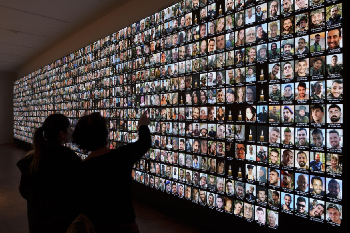 Visitors look at photos of Israeli people who were killed during Hamas militants attack on Oct. 7 and those who died during the Israel-Hamas war in the Gaza Strip, displayed on a giant screen at the National Library in Jerusalem, Israel, Sunday, Jan. 28, 2024.