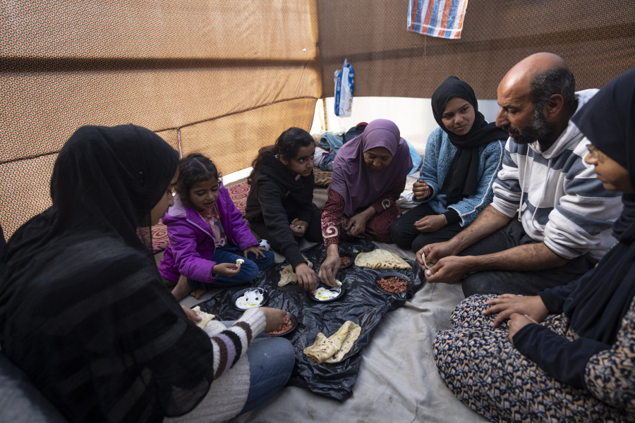Members of the Abu Jarad family, who were displaced by the Israeli bombardment of the Gaza Strip, eat breakfast at a makeshift tent camp in the Muwasi area, southern Gaza, Monday, Jan. 1, 2024.