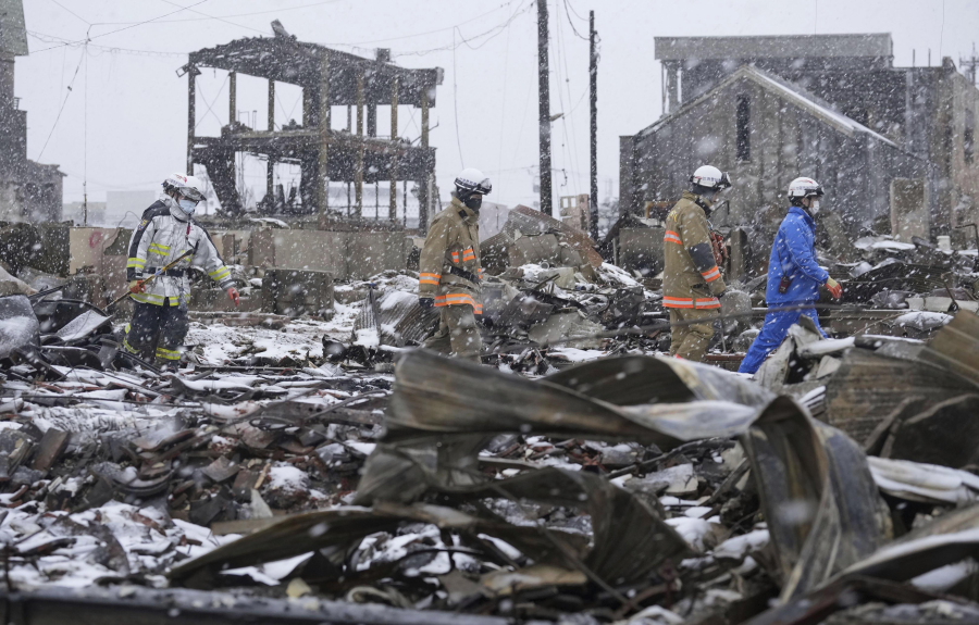 Snow falls as rescuers conduct a search operation around a burnt market in Wajima, Ishikawa prefecture, Japan Sunday, Jan. 7, 2024. A major earthquake slammed western Japan on Jan. 1, killing scores of people, toppling buildings and setting off landslides.