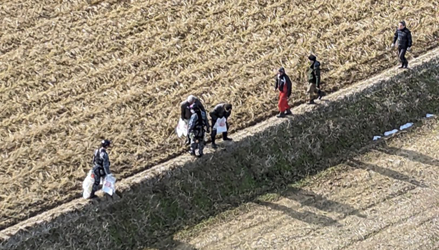 In this photo provided by Japanese Ministry of Defense,  Japan Self Defense Force members, left side, carry water in plastic bags, to hand over to local residents on the rice field in the quake-hit Wajima city, Ishikawa prefecture, Japan, Friday, Jan. 5, 2024.