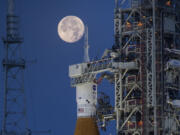 A full moon is seen behind the Artemis I Space Launch System (SLS) and Orion spacecraft, atop the mobile launcher, are prepared for a wet dress rehearsal to practice timelines and procedures for launch, at Launch Complex 39B at NASA&rsquo;s Kennedy Space Center in Florida on June 14, 2022. On Tuesday, Jan. 9, 2024, NASA said astronauts will have to wait until 2025 before flying to the moon and another few years before landing on it.