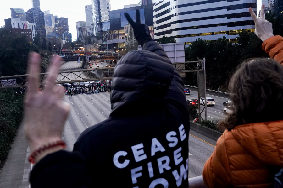 Protesters calling for a cease-fire in the Israel-Hamas war gesture a peace sign on an overpass to those below as they block Interstate 5 northbound Saturday, Jan. 6, 2024, in downtown Seattle.