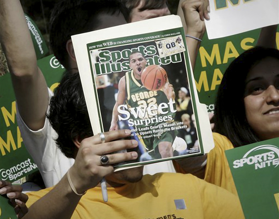 FILE - A George Mason University fan holds up the cover of Sports Illustrated magazine at a send off for the team, Wednesday, March 29, 2006, in Fairfax, Va. The publisher of Sports Illustrated has notified employees it is planning to lay off a significant portion &mdash; possibly all &mdash; of the outlet&rsquo;s staff after its license to use the iconic brand&rsquo;s name in print and digital was revoked. In an email to employees Friday morning, Jan. 19, 2024, the Arena Group, which operates Sports Illustrated and related properties, said that Authentic Brands Group has revoked its marketing license.