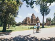 A woman rides a bicycle next to the Pre Rup temple ruins in Angkor Wat complex, Cambodia.