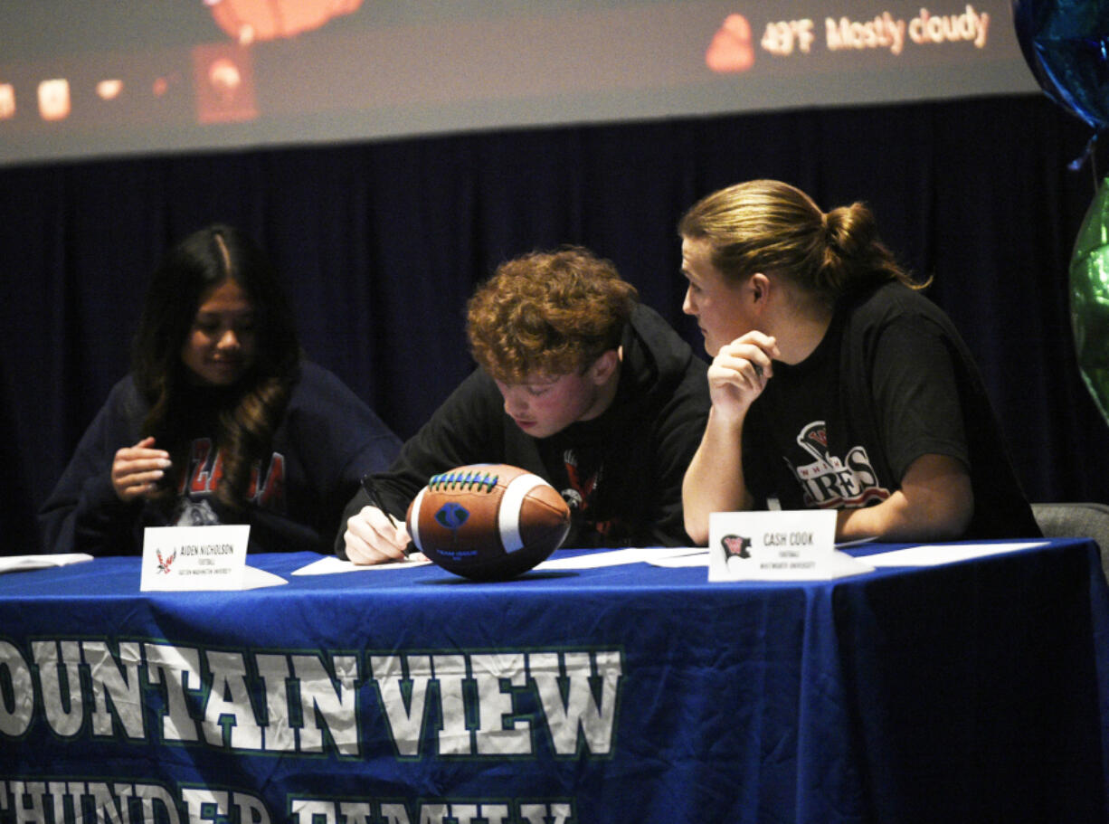 Mountain View seniors Aiden Nicholson (center) and Cash Cook sign papers during a College Signing Day ceremony at Mountain View High School on Wednesday, Feb. 7, 2024.