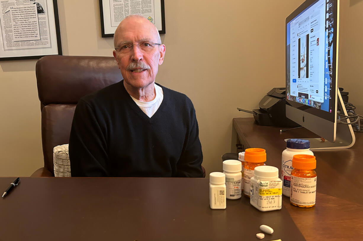 David Mitchell, founder of Patients for Affordable Drugs, sits in his home office. Beside him are some of the many drugs he takes to treat multiple myeloma and other conditions.