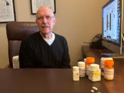 David Mitchell, founder of Patients for Affordable Drugs, sits in his home office. Beside him are some of the many drugs he takes to treat multiple myeloma and other conditions.