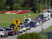 A line of vehicles wait to enter Canada at the Peace Arch border crossing in view of a Canadian flag made of flowers Aug. 9, 2021, in Blaine.