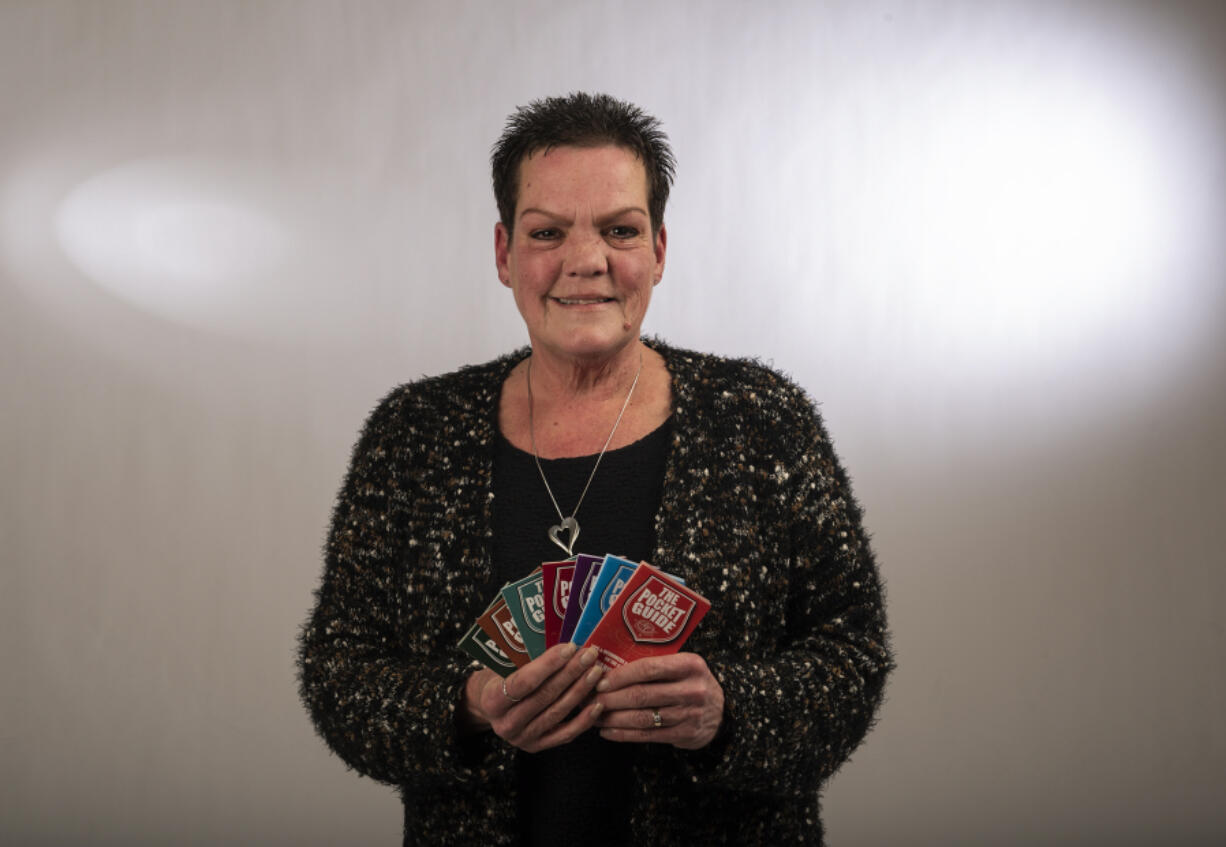 Pocket Guide creator Lois Smith stands for a portrait while holding various editions of the pamphlet Friday in The Columbian&rsquo;s newsroom. The books, which Smith began handing out in 2017, provide tips and key resource contact information for those living outside.