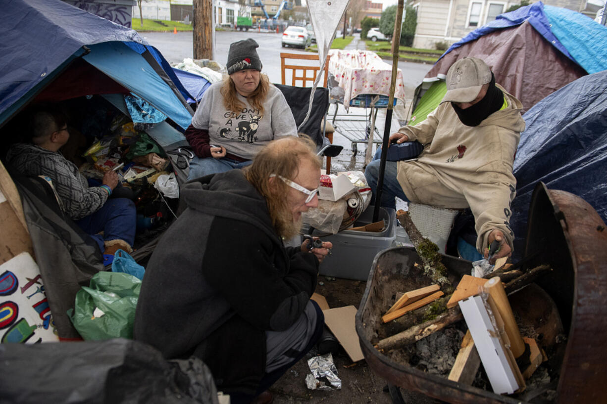 Cheri Rhodes, gray beanie, joins Mike Moises, white glasses, and other members of their street family as a small fire provides a little warmth in the pouring rain at their downtown Vancouver encampment on a recent afternoon.