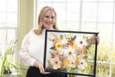 Daphne Andersons holds a completed, framed bouquet. Her business, Vancuterie, offers bridal bouquet preservation using ancient Japanese flower-pressing techniques.