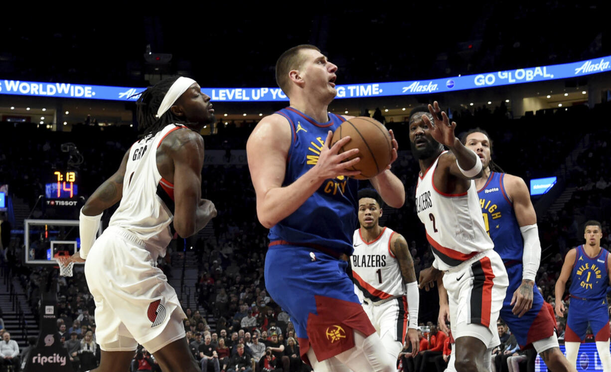 Denver Nuggets center Nikola Jokic, center, drives to the basket against Portland Trail Blazers forward Jerami Grant, left, and center Deandre Ayton, front right, during the first half of an NBA basketball game in Portland, Ore., Friday, Feb. 23, 2024.