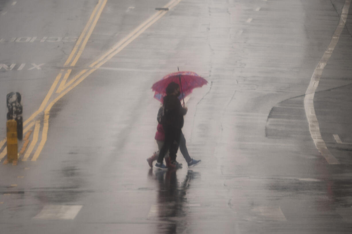 People cross the street with umbrellas in heavy rain in Los Angeles, Monday, Feb. 19, 2024.