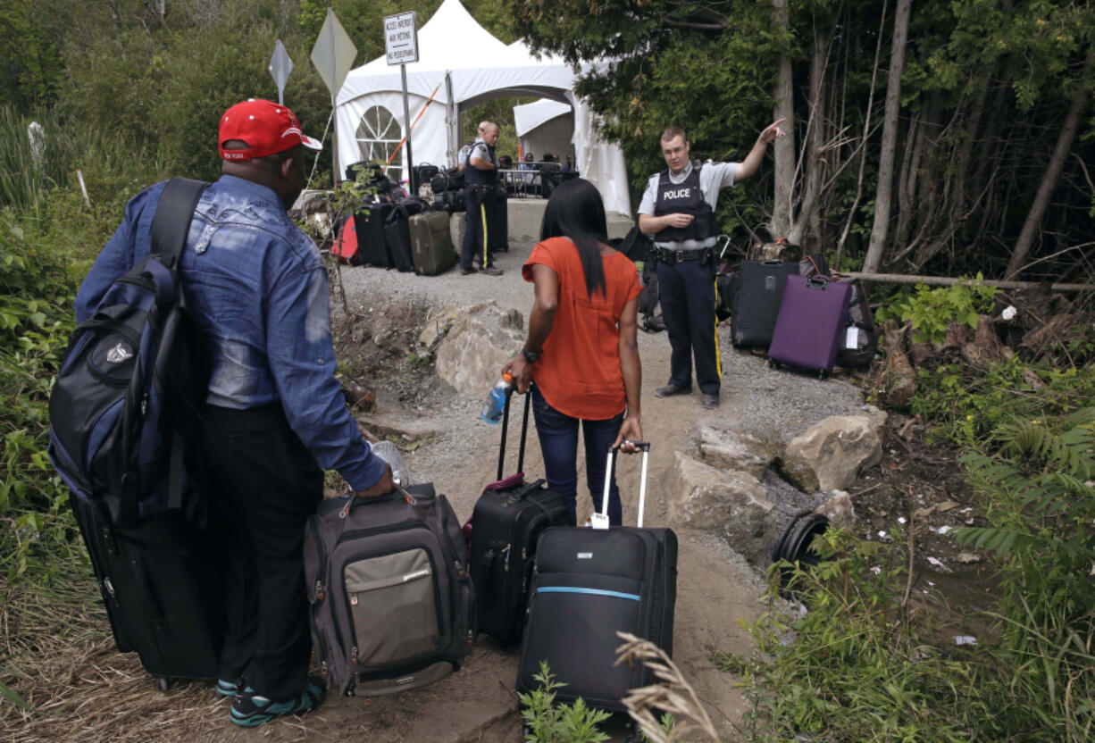 FILE - A Royal Canadian Mounted Police officer informs a migrant couple of the location of a legal border station, shortly before they illegally crossed from Champlain, N.Y., to Saint-Bernard-de-Lacolle, Quebec, using Roxham Road. Canada&rsquo;s government is reimposing some visa requirements on Mexican nationals visiting Canada, an official familiar with the matter told The Associated Press on Wednesday, Feb. 28, 2024. Quebec&rsquo;s premier has been urging the federal government to slow the influx of refugees which he says has been straining resources.