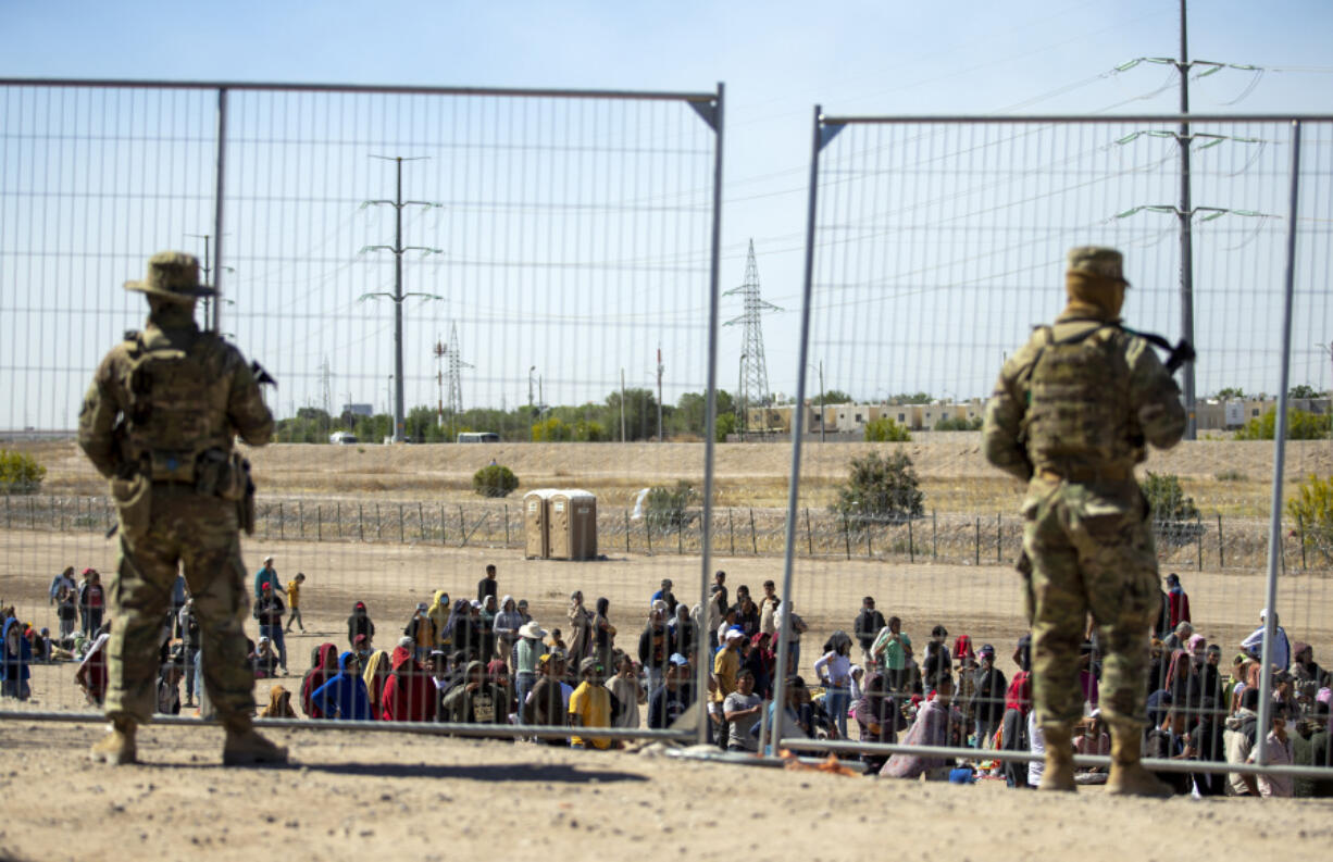FILE - Migrants wait in line adjacent to the border fence under the watch of the Texas National Guard to enter into El Paso, Texas, May 10, 2023. Senators are racing to release a highly-anticipated bill that pairs border enforcement policy with wartime aid for Ukraine, Israel and other U.S. allies, as part of a long-shot effort to push the package through heavy skepticism from Republicans, including House Speaker Mike Johnson.