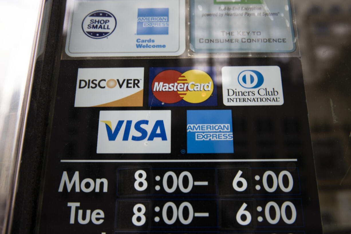 File - Credit card options are shown on a store&rsquo;s door on Nov. 29, 2018 in Philadelphia. Noticeable pockets of Americans are quickly running up their credit card balances and increasing numbers are now falling behind on their debts.