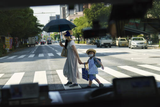 FILE - A pedestrian crossing a street with a child is seen through a taxi window in Tokyo, Monday, July 19, 2021.  The number of babies born in Japan last year fell for an eighth straight year to a new low, government data showed Tuesday, Feb. 27, 2024, and a top official said it was critical for the country to reverse the trend in the coming half-dozen years.