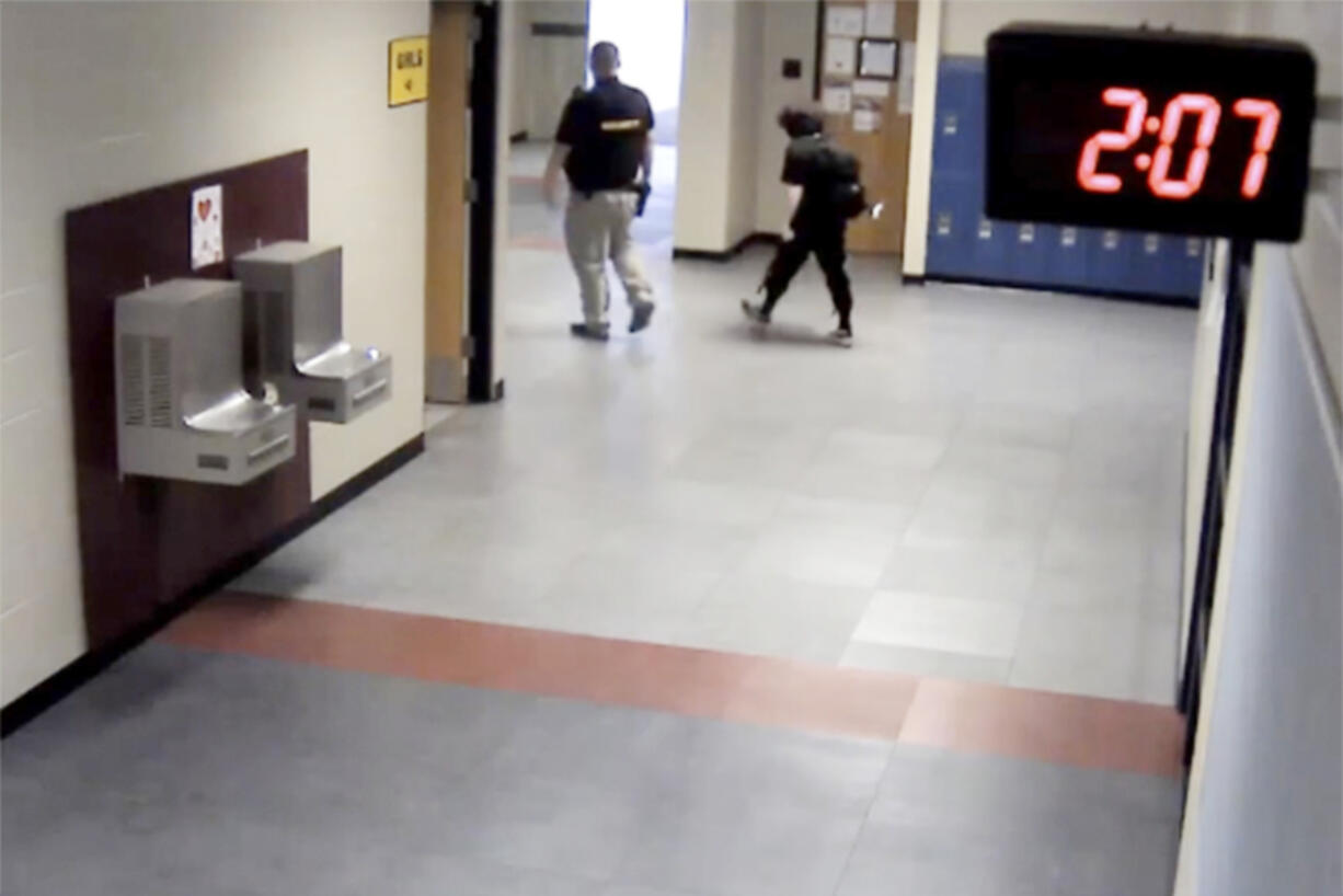 In this image taken from video taken from a school security camera and provided by the Owasso Police Dept., Nex Benedict is seen walking out of the school with a security guard, Feb. 7, 2024, at Owasso High School in Owasso, Okla. A recently released police search warrant is revealing more details in the case of a Benedict, a nonbinary student, who died a day after a high school bathroom fight.