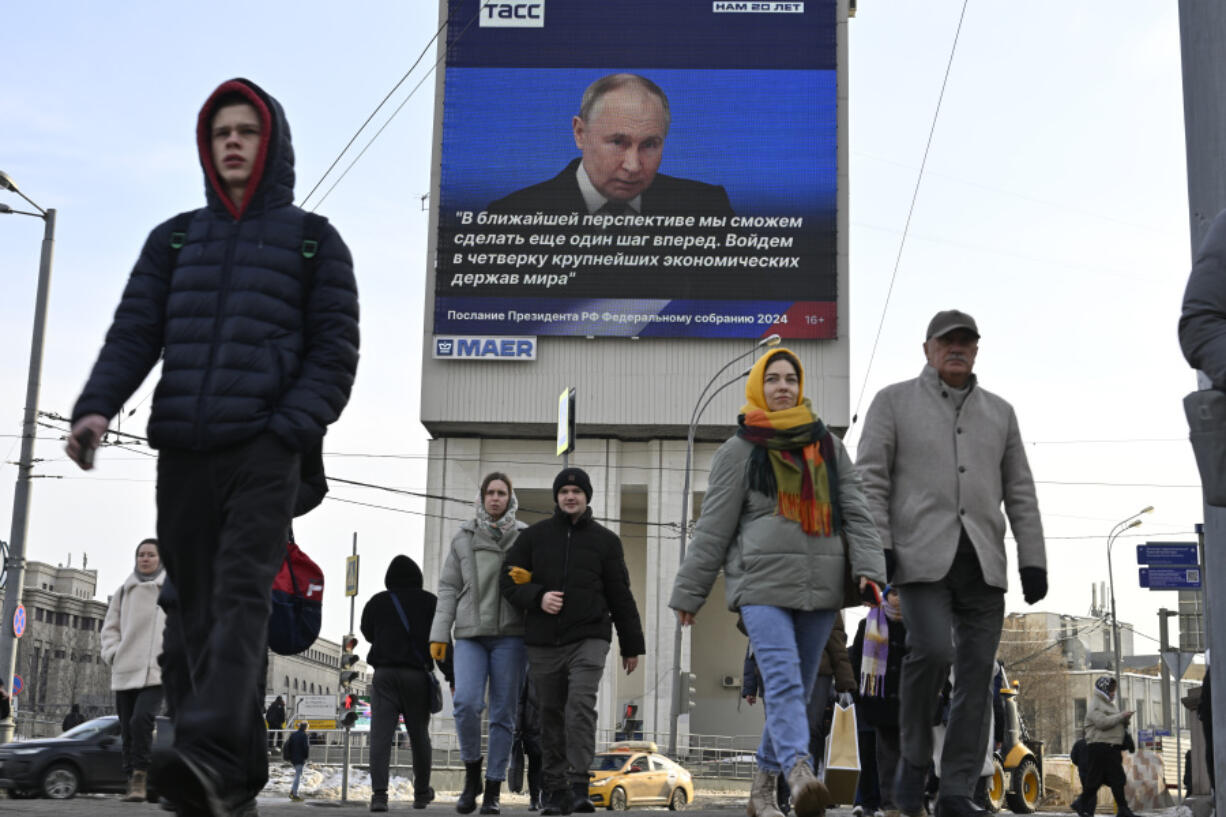 People walk past an electronic billboard on a building showing Russian President Vladimir Putin as he gives his annual state-of-the-nation address in Moscow, Russia, on Thursday, Feb. 29, 2024.