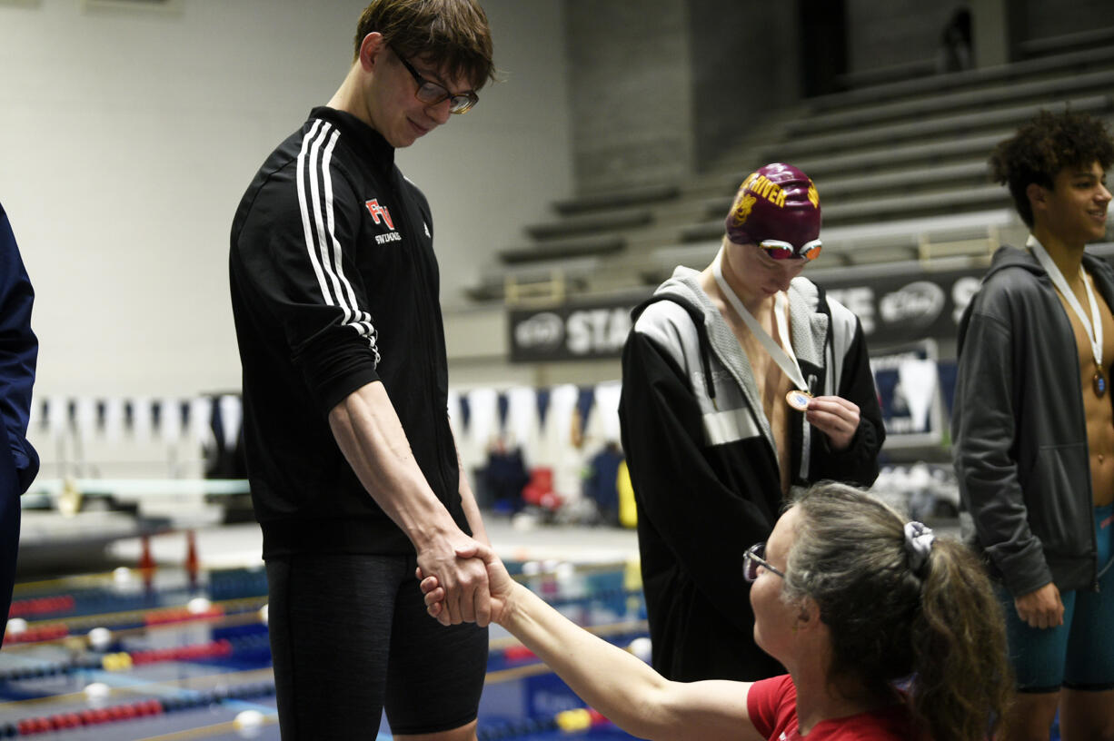 Tarik Kurta of Fort Vancouver shakes the hand of his coach Sarah Dunn on the podium after finishing second in the 50 freestyle at the 2A boys swimming state championship meet at the King County Aquatic Center in Federal Way on Saturday, Feb. 17, 2024.