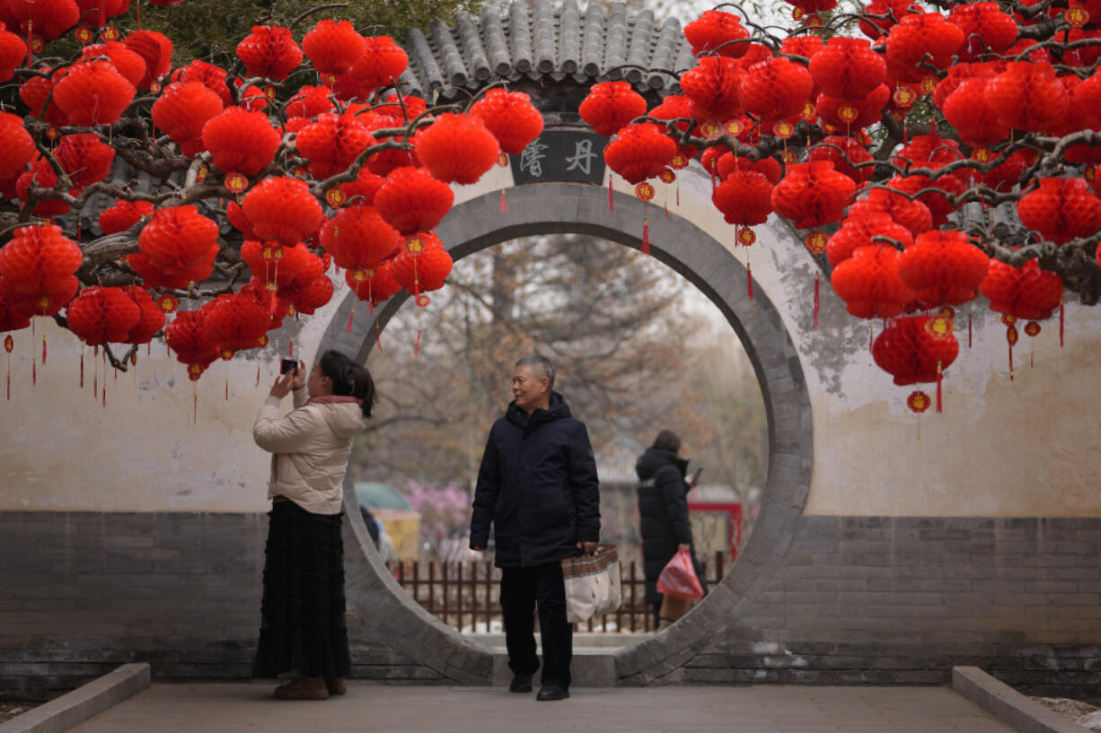 Residents take souvenir photos of a tree decorated with red lanterns Sunday ahead of the Chinese Lunar New Year at Ditan Park in Beijing.