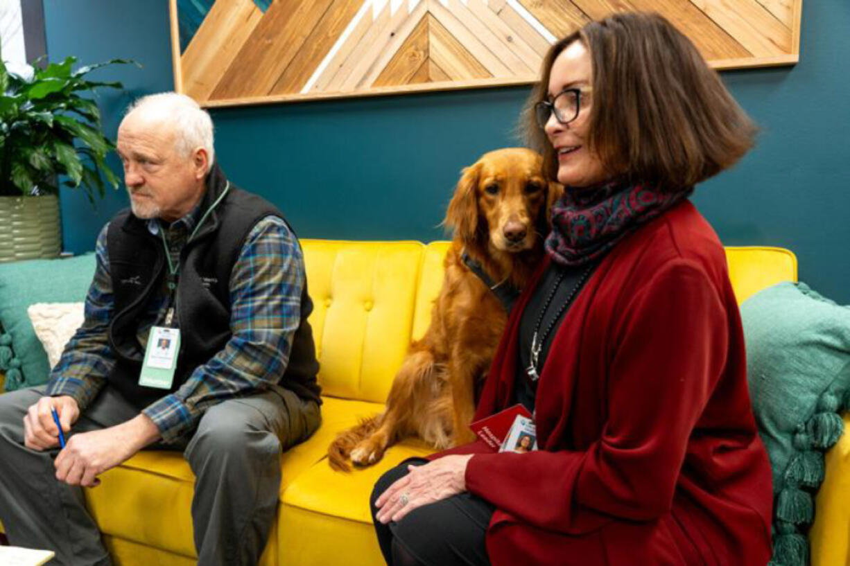 Lily, a therapy dog at CHI Mercy Medical Center in Roseburg, Ore., sits Thursday between her owner, Chuck Allured, left, and CHI Mercy Health director of volunteer services Teresa Scott.