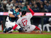 Seattle Mariners catcher Cal Raleigh can't get a tag on Boston Red Sox's Tyler O'Neill, who scored on a throwing error by Mariners third baseman Josh Rojas during the fourth inning of an opening-day baseball game Thursday, March 28, 2024, in Seattle.