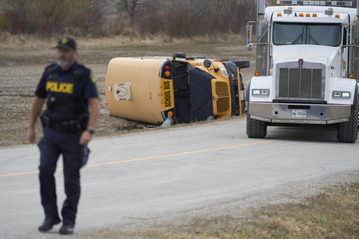 An OPP officer walks past a school bus which rolled over south of Woodstock, Ontario, Canada, on Tuesday, March 5, 2024. A number of students were injured after a school bus carrying 40 children rolled over.