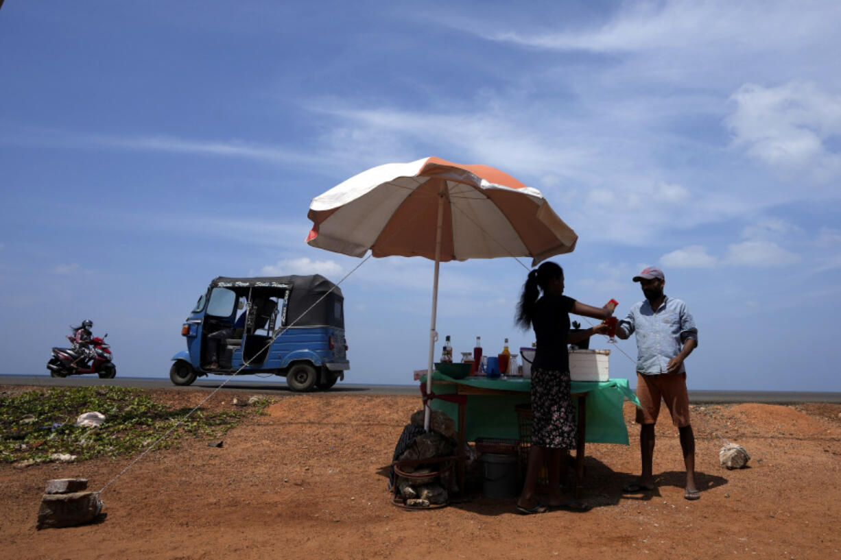FILE - A man buys a cool drink from a roadside vendor on a sunny day in Mahawewa, a village north of Colombo, Sri Lanka, Feb. 29, 2024. Earth has exceeded global heat records in February, according to the European Union climate agency Copernicus.