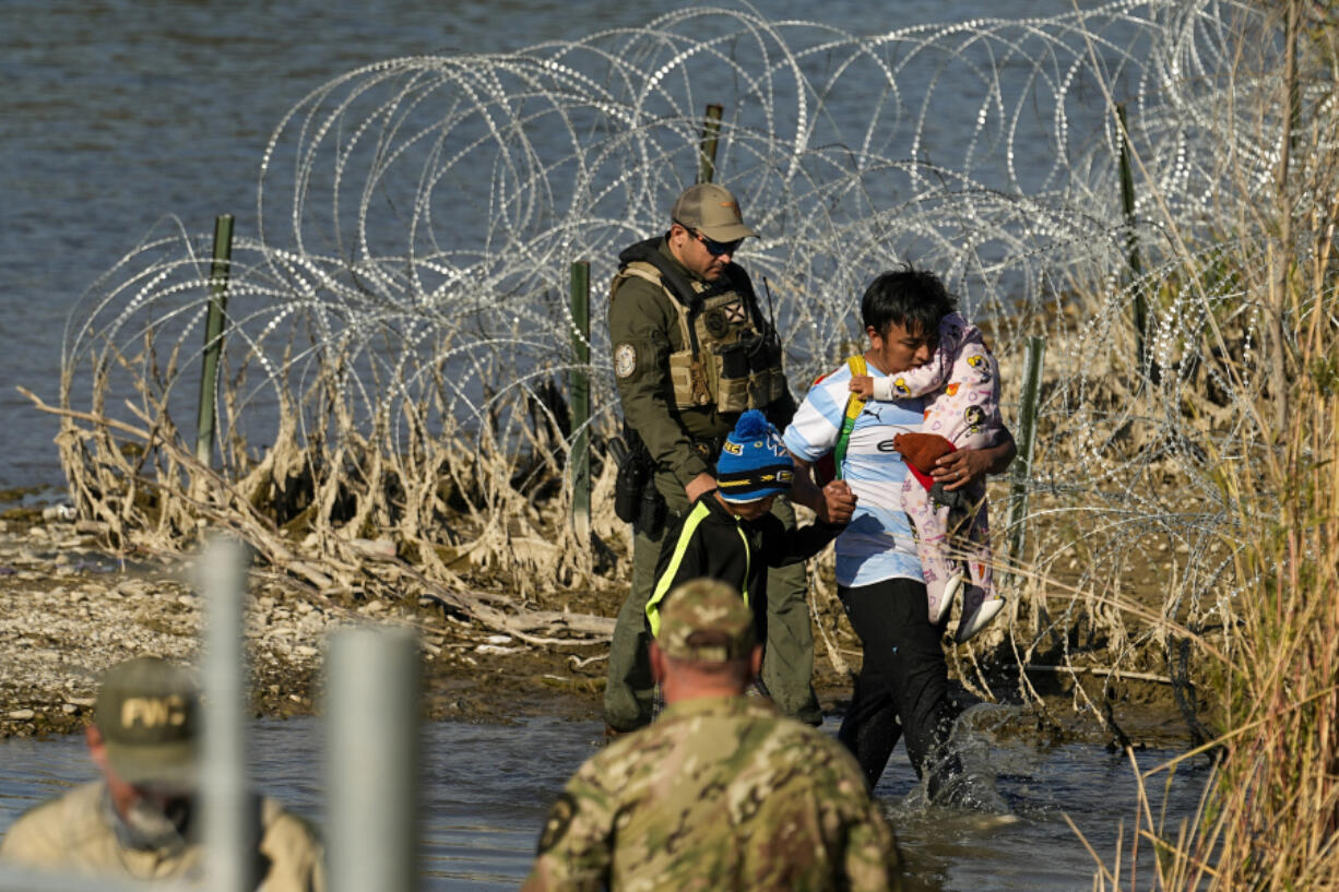 FILE - Migrants are taken into custody by officials at the Texas-Mexico border, Jan. 3, 2024, in Eagle Pass, Texas. The Supreme Court on Tuesday, March 12, 2024 extended a stay on a new Texas law that would empower police to arrest migrants suspected of illegally crossing the U.S.-Mexico border.  The order puts the law on hold until at least Monday while the high court considers a challenge by the Justice Department, which has called the law an unconstitutional overreach.