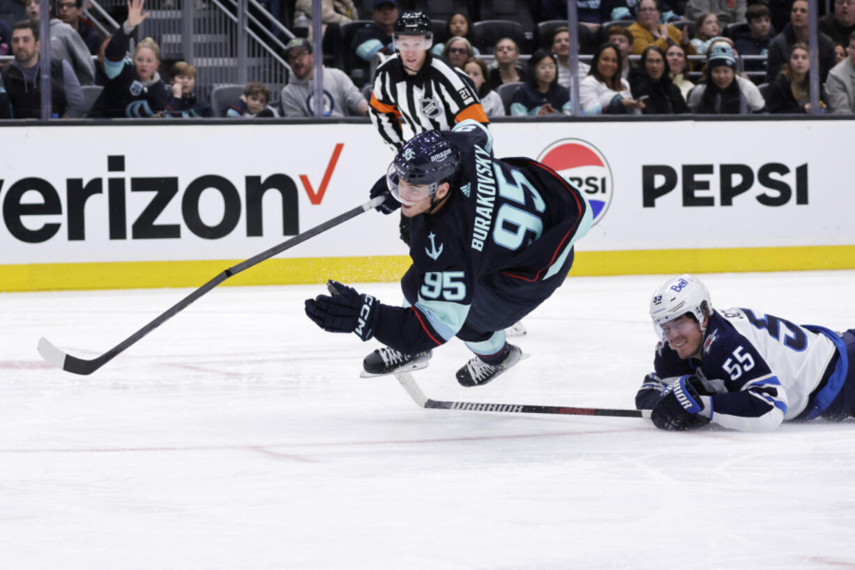 Seattle Kraken left wing Andre Burakovsky (95) goes down with Winnipeg Jets center Mark Scheifele (55) called for tripping during the third period of an NHL hockey game, Friday, March 8, 2024, in Seattle. The Jets won 3-0.