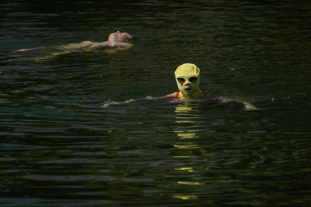FILE - A woman wearing sun protection headgear and sunglasses swims as residents cool off on a sweltering day at an urban waterway in Beijing, July 10, 2023. Climate change is making heat waves crawl slower across the globe and last longer with higher temperatures over larger areas, a new study finds.
