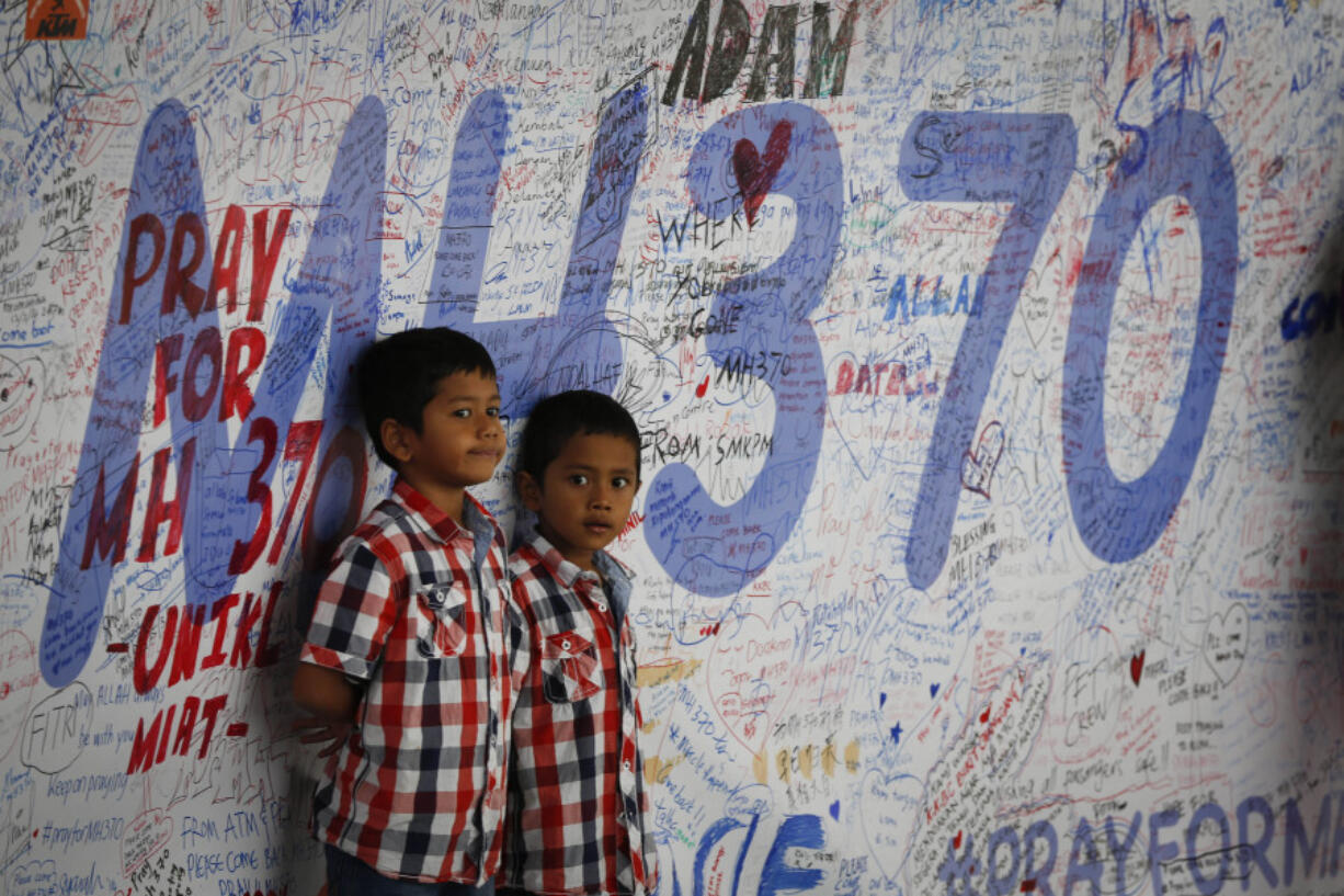 FILE - Two Malaysian children stand in front of a messages board and well wishes on it to people involved with the missing Malaysia Airlines jetliner MH370, in Sepang, Malaysia, on March 16, 2014. A decade ago this week, a Malaysia Airlines flight vanished without a trace to become one of aviation&rsquo;s biggest mystery. Investigators still do not know exactly what happened to the plane and its 239 passengers.