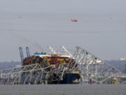 A helicopter flies over a container ship as it rests against wreckage of the Francis Scott Key Bridge on Tuesday, March 26, 2024, as seen from Pasadena, Md.  The ship rammed into the major bridge in Baltimore early Tuesday, causing it to collapse in a matter of seconds and creating a terrifying scene as several vehicles plunged into the chilly river below.