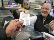 FILE - Dot Skoko, owner of Dot&rsquo;s Dollar More or Less shop in Mt. Lebanon, Pa., hands a customer a Mega Millions lottery ticket, Thursday, Jan. 5, 2022. The Mega Millions jackpot has reached an astounding $977 million for Friday night&rsquo;s drawing after no tickets matched all six numbers drawn on Tuesday night. (AP Photo/Gene J.