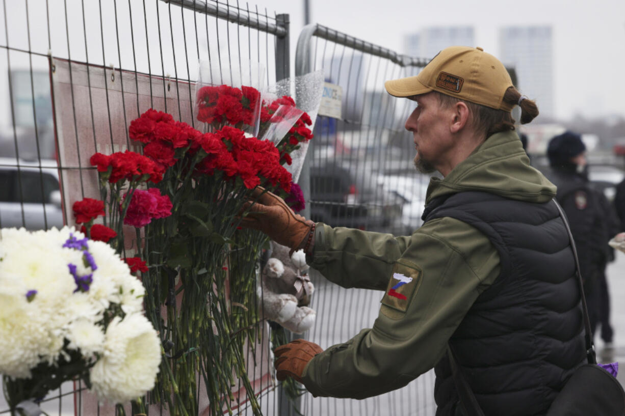 A man places flowers on the fence near the Crocus City Hall on the western edge of Moscow, Russia, Saturday, March 23, 2024, following an attack Friday, for which the Islamic State group claimed responsibility.  Over 90 people were killed, including at least three children, authorities said.