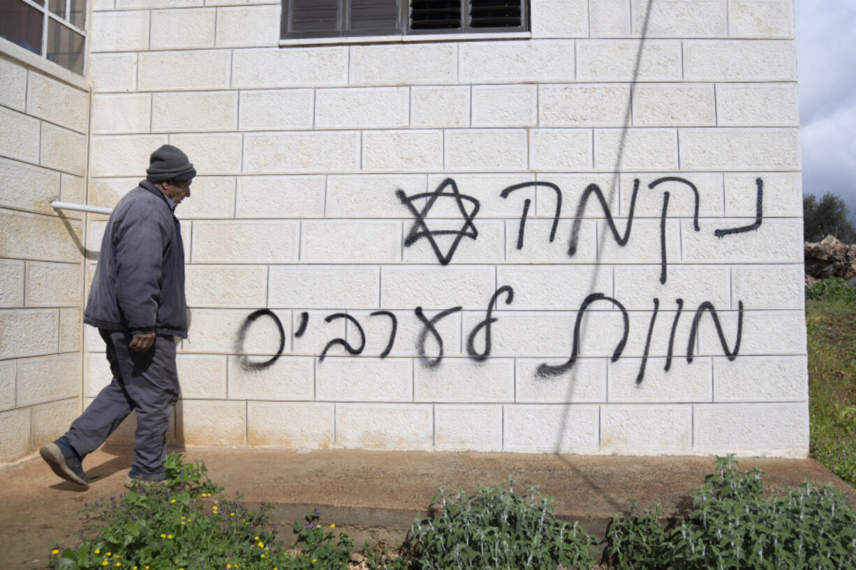 FILE - A man looks at graffiti that reads, in Hebrew, &ldquo;revenge, death to Arabs,&rdquo; allegedly sprayed by Jewish West Bank settlers in the Palestinian West Bank village of Turmus Ayya, Feb. 18, 2024. The U.S. has imposed sanctions on a group of three extremist Israeli West Bank settlers who are accused of harassing and attacking Palestinians in an attempt to pressure them to leave their land.