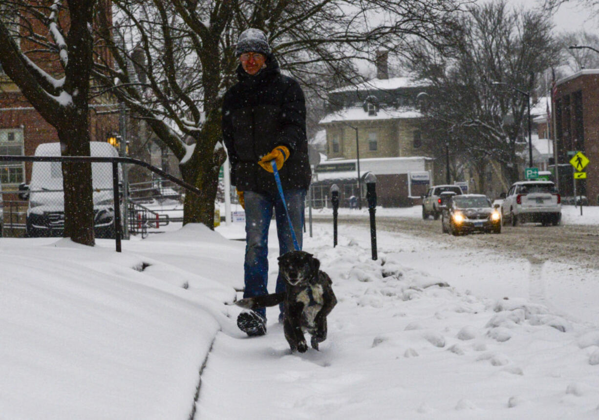 A man walks his dog down Main Street in Brattleboro, Vt., on Saturday, March 23, 2024.  New England is battling a mix of wind, rain, sleet and heavy snow across the region Saturday with more than a foot of snow expected in ski county, but mostly rain, wind and possible flooding in southern areas and along the coast.