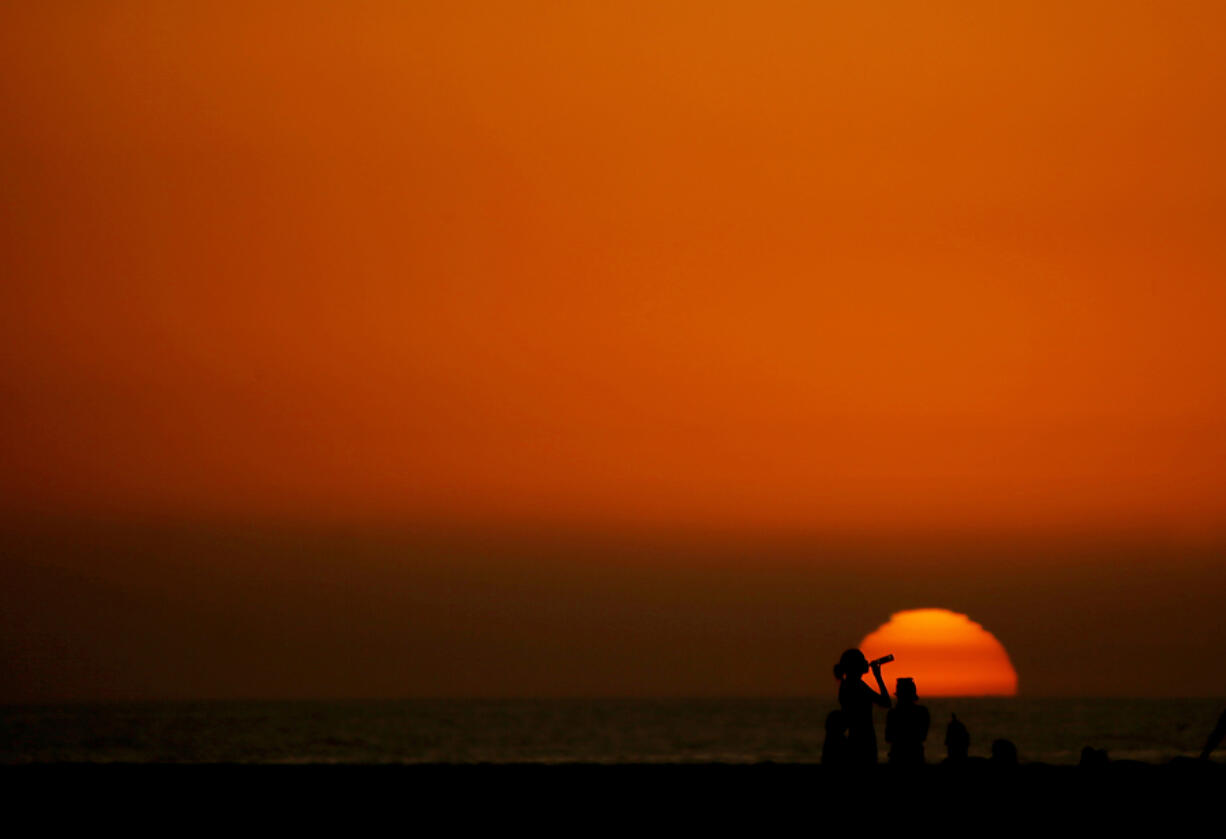 Beachgoers are framed against the setting sun at the end of a warm day Dec. 6 in Huntington Beach, Calif. Last year&rsquo;s global average temperature of 58.96 degrees was about a third of a degree warmer than the previous hottest year in 2016.