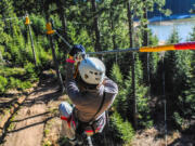 A woman glides down a zip line over a wooded area. The Catamount Zip Tour transports riders from the top of a mountain via a cable suspended hundreds of feet above the trees, a 5,523-foot line, a bit more than a mile.