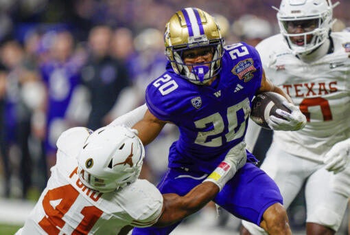 FILE - Texas linebacker Jaylan Ford (41) tries to tackle Washington running back Tylin "Tybo" Rogers (20) during the Sugar Bowl CFP NCAA semifinal college football game, Jan. 1, 2024, in New Orleans. Rogers was arrested Friday, April 5, and charged Tuesday, April 9, with raping two women in Seattle. Court documents say he played in two College Football Playoff games for the school after the allegations were known to the university.  (AP Photo/Jacob Kupferman, File)