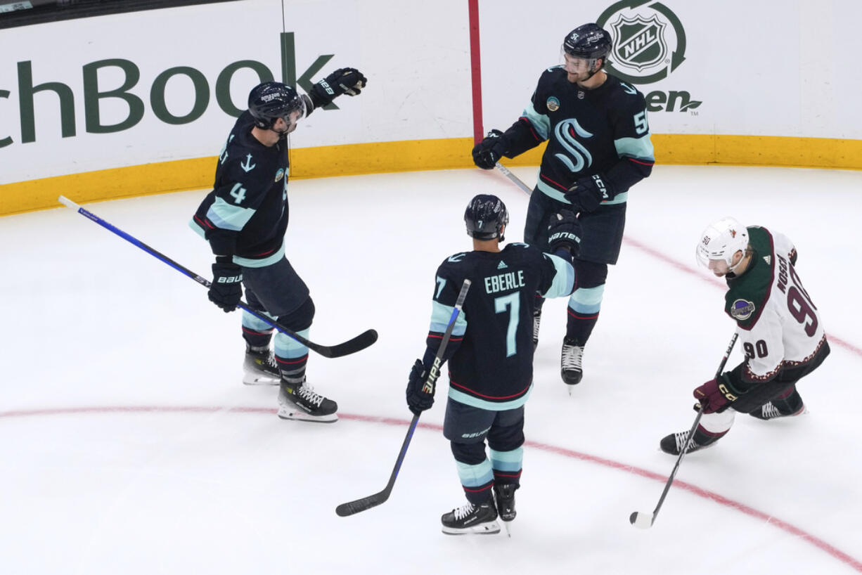 Seattle Kraken center Shane Wright, top right, celebrates his goal with Justin Schultz (4) and Jordan Eberle (7) as Arizona Coyotes defenseman J.J. Moser, right, skates away during the first period of an NHL hockey game Tuesday, April 9, 2024, in Seattle.