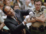 FILE - In this June 15, 1995 file photo, O.J. Simpson, left, grimaces as he tries on one of the leather gloves prosecutors say he wore the night his ex-wife Nicole Brown Simpson and Ron Goldman were murdered in a Los Angeles courtroom. Simpson, the decorated football superstar and Hollywood actor who was acquitted of charges he killed his former wife and her friend but later found liable in a separate civil trial, has died.