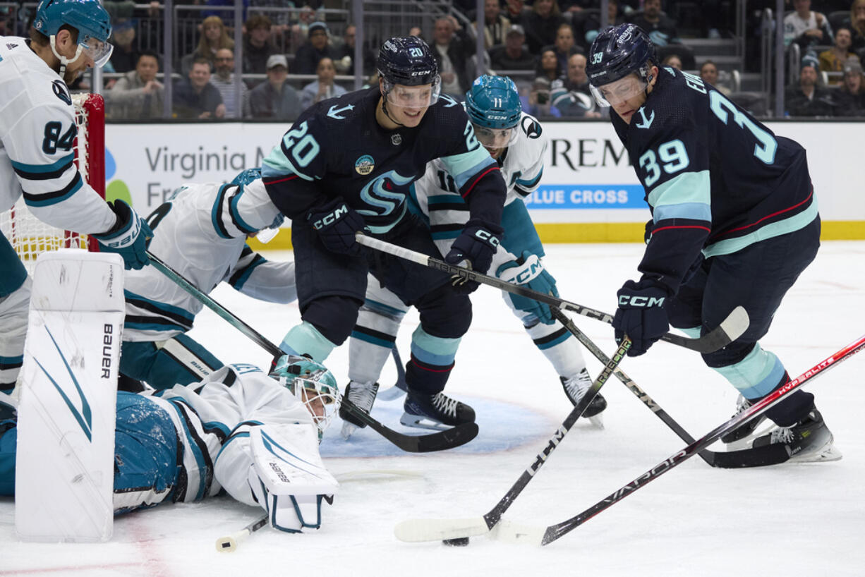 Seattle Kraken defenseman Ryker Evans (39) reaches for the puck on a shot blocked by San Jose Sharks goaltender Devin Cooley, bottom left, with Kraken right wing Eeli Tolvanen (20) assisting during the first period of an NHL hockey game, Thursday, April 11, 2024, in Seattle.