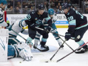 Seattle Kraken defenseman Ryker Evans (39) reaches for the puck on a shot blocked by San Jose Sharks goaltender Devin Cooley, bottom left, with Kraken right wing Eeli Tolvanen (20) assisting during the first period of an NHL hockey game, Thursday, April 11, 2024, in Seattle.