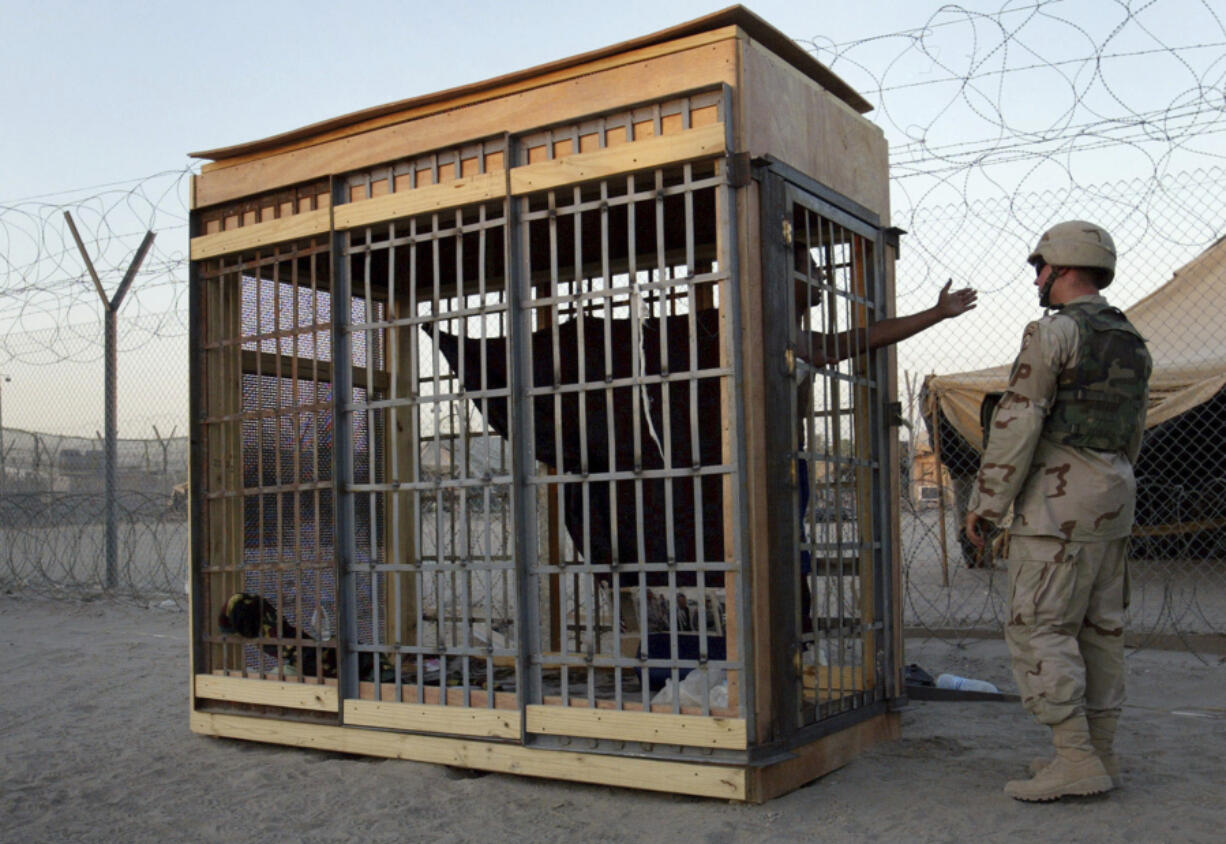 FILE - In this June 22, 2004, photo, a detainee in an outdoor solitary confinement cell talks with a military police officer at the Abu Ghraib prison on the outskirts of Baghdad, Iraq. A trial scheduled to begin Monday, April 15, 2024, in U.S. District Court in Alexandria, Va., will be the first time that survivors of Iraq&rsquo;s Abu Ghraib prison will bring their claims of torture to a U.S. jury. Twenty years ago, photos of abused prisoners and smiling U.S. soldiers guarding them shocked the world.