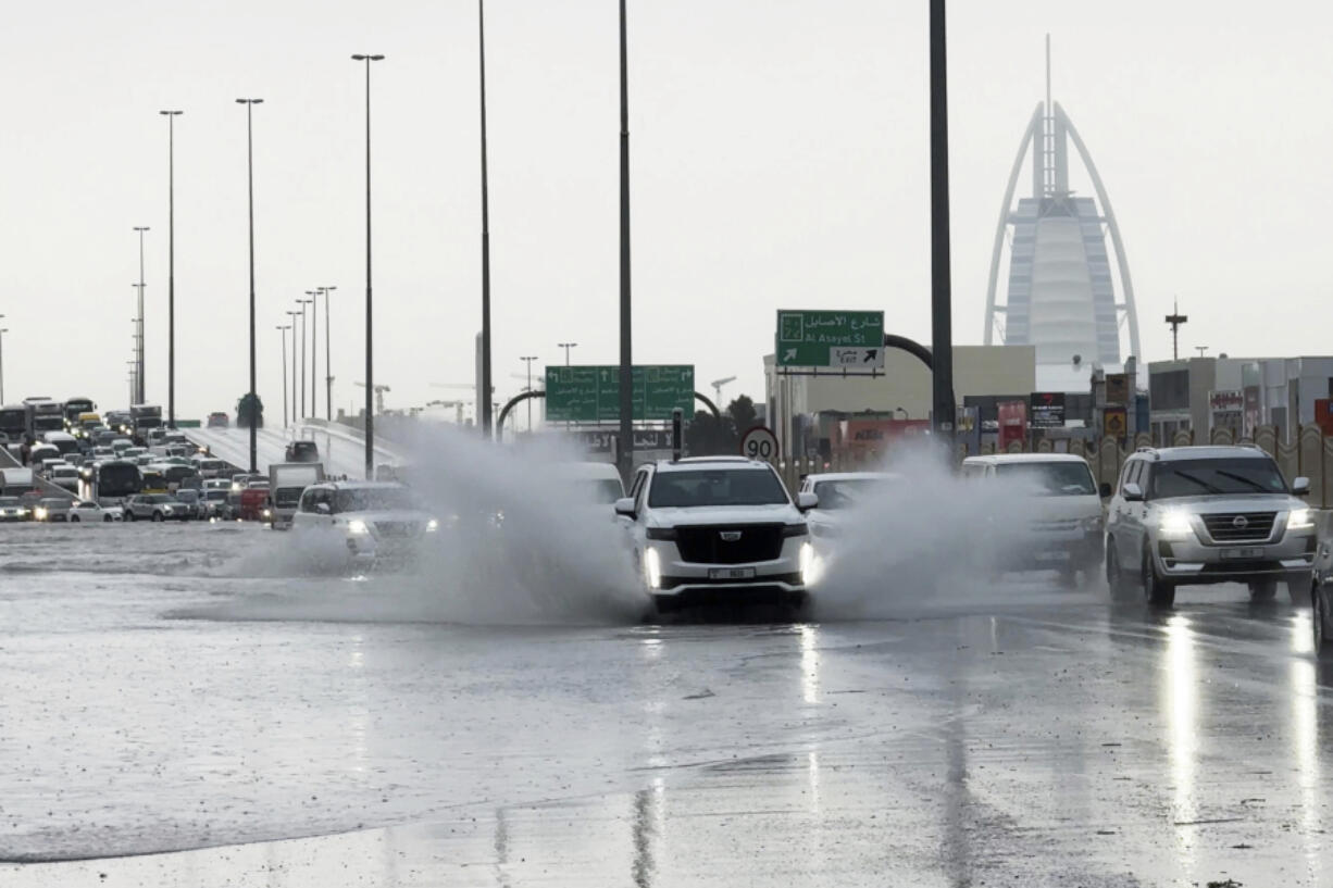 An SUV splashes through standing water on a road with the Burj Al Arab luxury hotel seen in the background in Dubai, United Arab Emirates, Tuesday, April 16, 2024. Heavy rains lashed the United Arab Emirates on Tuesday, flooding out portions of major highways and leaving vehicles abandoned on roadways across Dubai. Meanwhile, the death toll in separate heavy flooding in neighboring Oman rose to 18 with others still missing as the sultanate prepared for the storm.