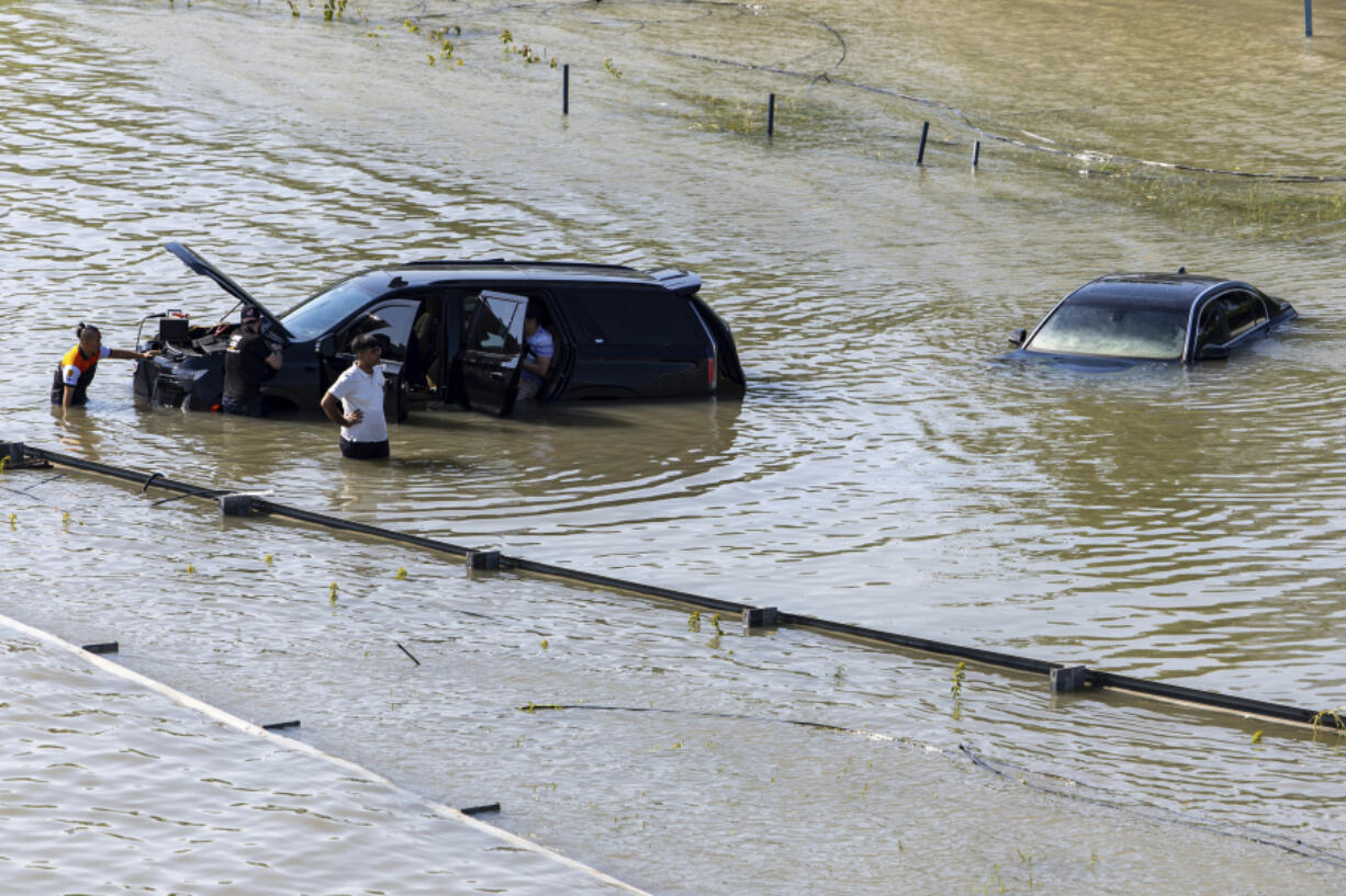 A group of people work to recover an abandoned vehicle taken by floodwater caused by heavy rain in Dubai, United Arab Emirates, Thursday, April 18, 2024. The United Arab Emirates attempted to dry out Thursday from the heaviest rain the desert nation has ever recorded, a deluge that flooded out Dubai International Airport and disrupted flights through the world&rsquo;s busiest airfield for international travel.