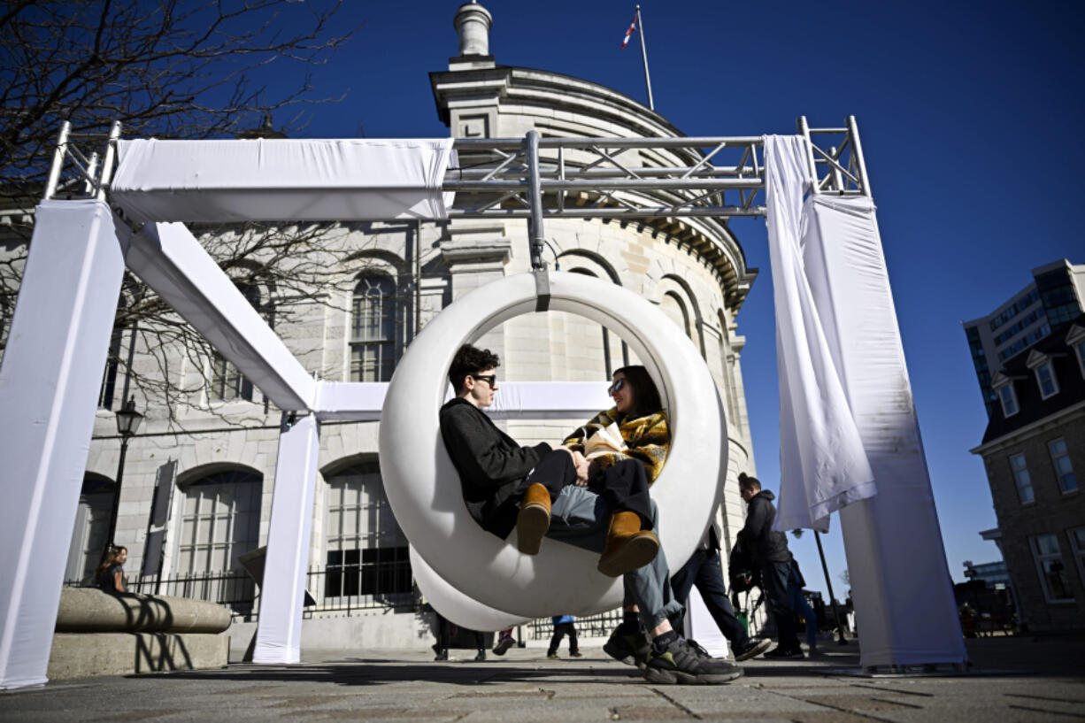 Antoine Gregoire, left, and Bella Crysler lounge in a furniture installment in the shape of an eclipse at Springer Market Square, a day before a total solar eclipse will be visible in Kingston, Ontario, Sunday, April 7, 2024.